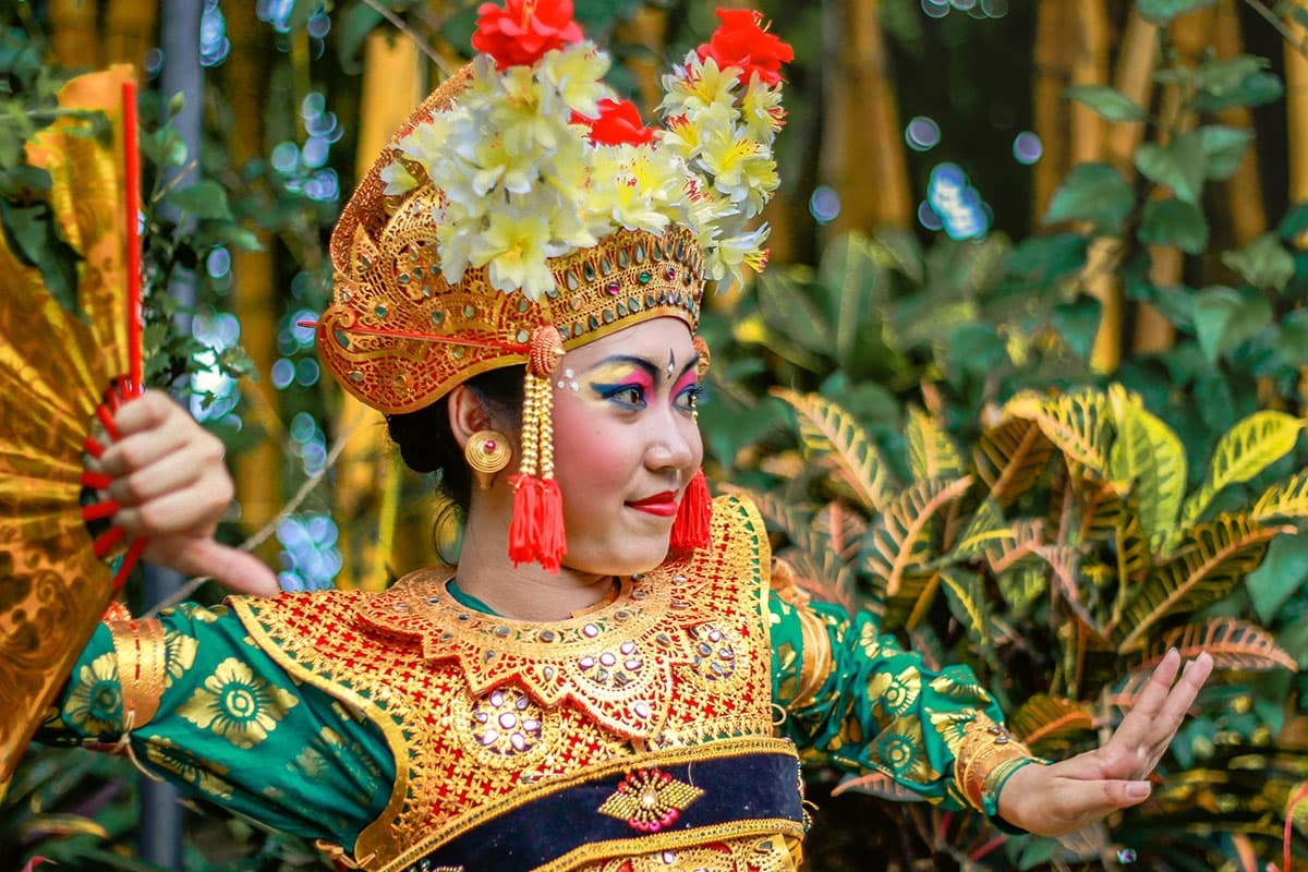 Balinese dancer in colorful traditional costume performing Joged Bungbung dance in tropical garden setting.