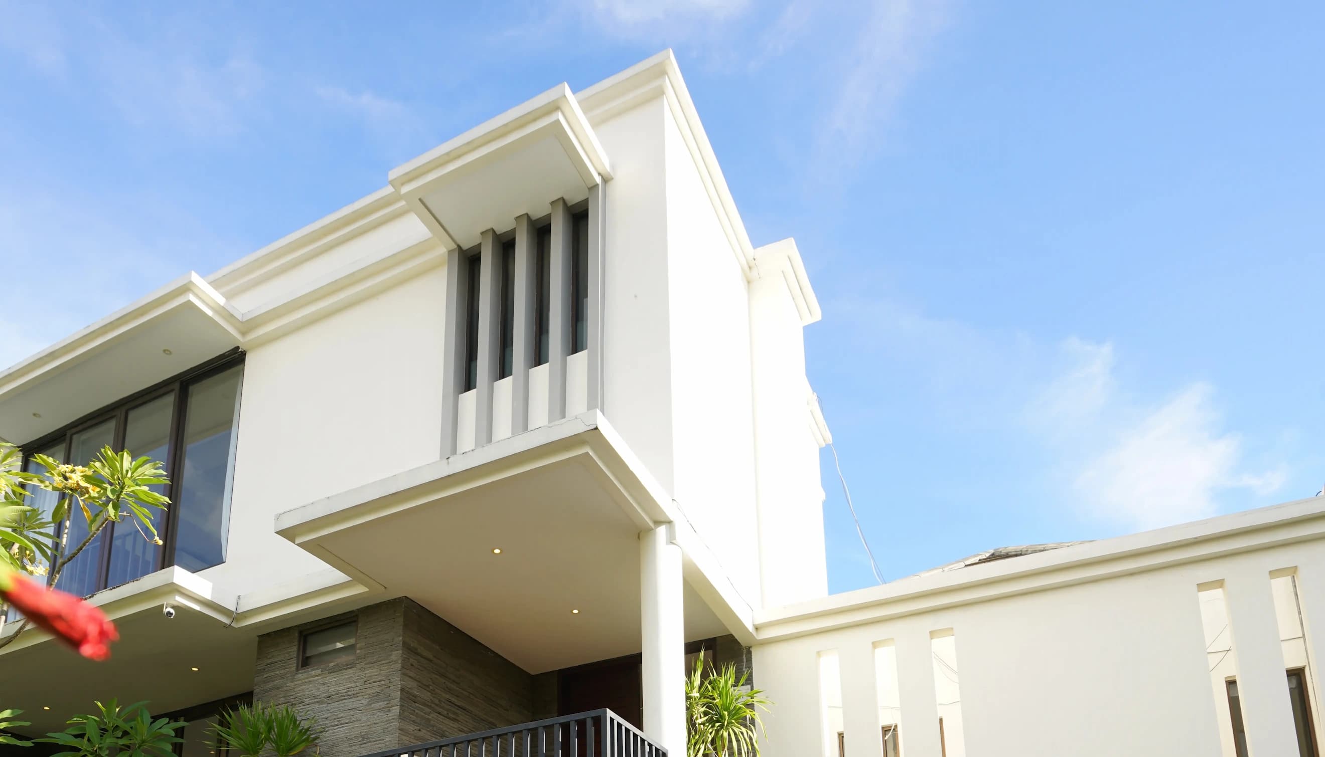 Modern facade of Villa Angan Angan in Canggu, Bali—white exterior with vertical windows, blue sky, and tropical plants.