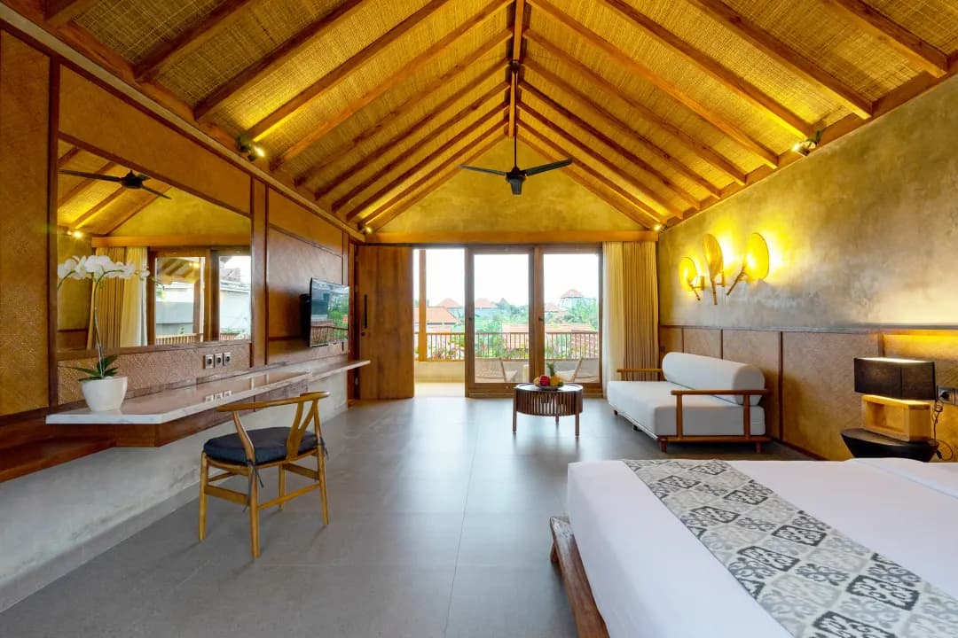 Spacious bedroom three at Jiwoku Villas Canggu Bali featuring bamboo ceiling, modern wooden furniture, lounge sofa, and balcony with tropical garden view