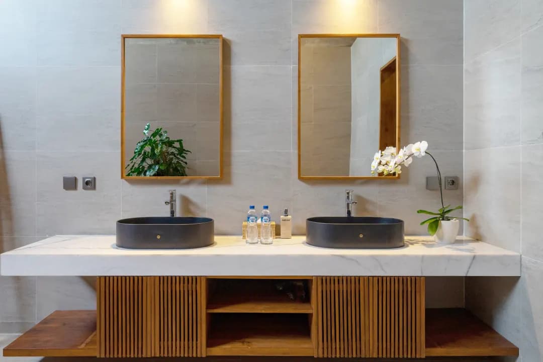 Spacious bathroom in bedroom three at Jiwoku Villas Canggu Bali featuring double sink vanity with marble top, wooden mirrors, bamboo towel ladder, and natural light design