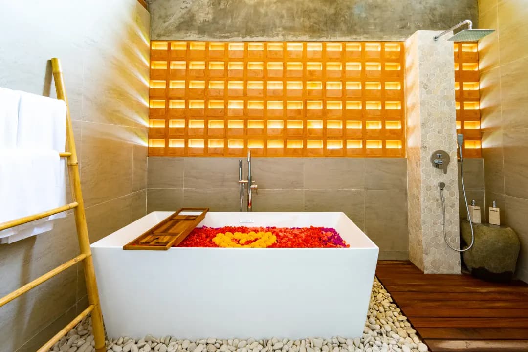 Modern bathroom in bedroom three at Jiwoku Villas Canggu Bali with square bathtub filled with flower petals and rain shower beside wooden platform