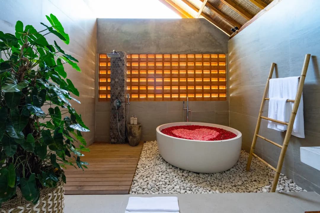 Open-style bathroom in bedroom three at Jiwoku Villas Canggu Bali with flower petal bathtub, rain shower, and natural light under wooden roof